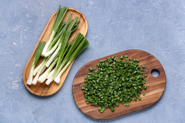 Boards with slices and fresh green onion on blue background