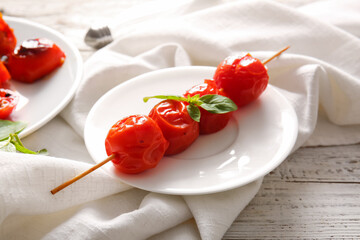 Skewer with tasty grilled tomatoes and basil on white wooden background