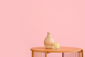 Wooden coffee table with vase and candle near pink wall