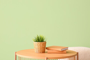 Wooden coffee table with houseplant, books and pouf near green wall