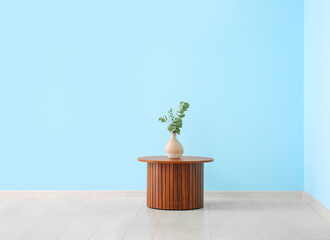 Wooden coffee table with eucalyptus branches in vase near blue wall