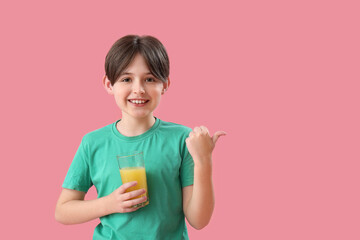 Little boy with glass of orange juice pointing at something on pink background