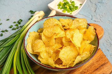 Bowl of tasty sour cream with sliced green onion and potato chips on blue background