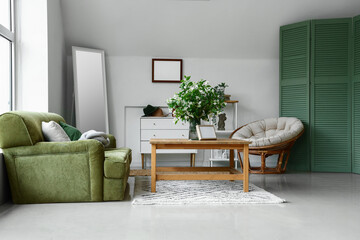 Interior of light living room with green sofa and blooming jasmine flowers on coffee table