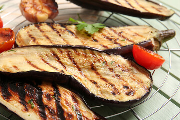 Cooling rack with delicious grilled eggplants and tomatoes on wooden background, closeup