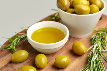 Bowls with ripe olives and oil on grey background