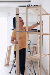 Woman assembling new wooden shelf and furniture in the apartment.