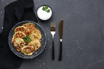 Bowl with tasty zucchini fritters and sour cream on grunge background