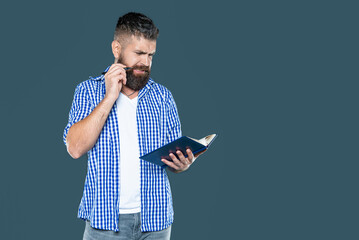 confused bearded man making notes in book on grey background