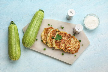 Board of tasty zucchini fritters with sour cream on light background