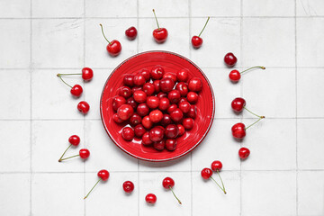 Plate with sweet cherries on white tile background