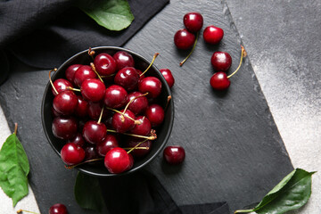 Board with bowl of sweet cherries on table