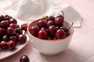 Plate and bowl with sweet cherries on pink tile table