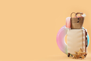 Suitcase with inflatable ring, starfishes and bag full of beach accessories on pale orange background. Travel concept