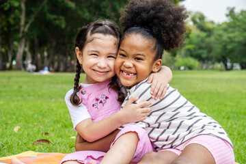 Two African American cheerful little girl sitting on the mat and hugging each other with love in the garden - Powered by Adobe