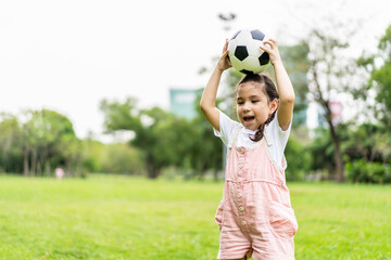 Smiling little girl standing holding the soccer ball at green football field in summer day....