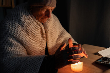 Freezing old man in winter clothes warms his hands over candle as energy blackouts cause...