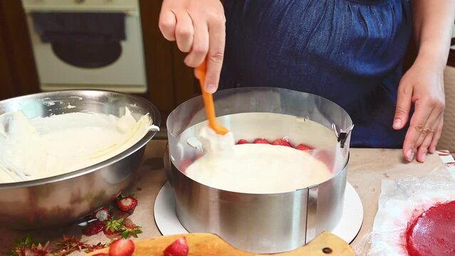 Close-up view of a chef pastry, baker, cook, confectioner , housewife putting whipped cream, preparing homemade delicious appetizing strawberry summer mousse cake - French mousse dessert Fraisier