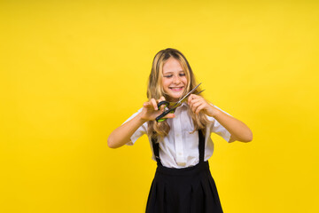 A young girl about to cut her own hair with a pair of scissors, isolated against yellow background