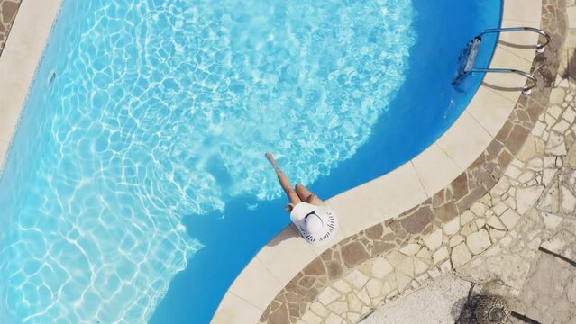Aerial view of a young woman sitting on the edge of a swimming pool