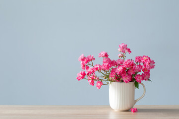 pink roses in ceramic vase on blue  background