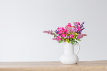 beautiful flowers in white jug on wooden shelf
