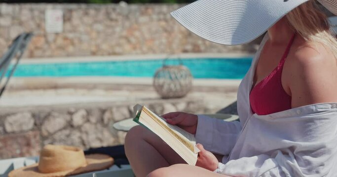 A young woman is reading a book near the swimming pool

