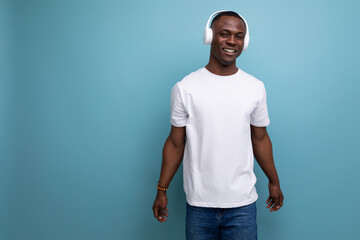 young african man in white t-shirt listening to music with white headphones on studio background with copy space