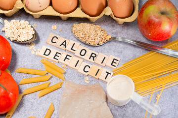 the inscription calorie deficit next to healthy food products. Flat lay photo showing weight loss and getting in shape - obrazy, fototapety, plakaty