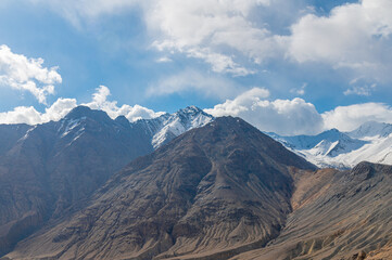 Fototapeta premium The barren landscape of Leh, Ladakh. Landscape view of rocky land surrounded by snow-covered Himalayas and Dramatic clouds.