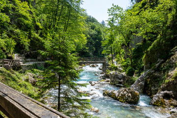 Fototapeta na wymiar Tourists walking over wooden bridge, suspended over wonderful Soca river tributary, deep in the slovenian Alps