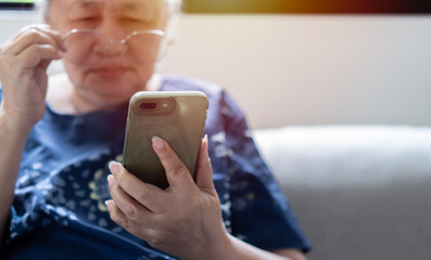 Asian senior fatigue woman taking off eye glasses during using smartphone after surfing internet at home