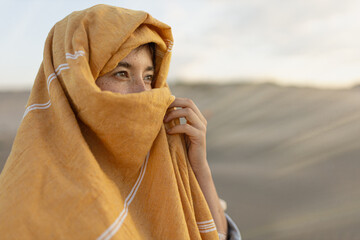 woman in the desert on expedition with his face covered against the light at sunset looking at the camera, in the golden light, traveling the world