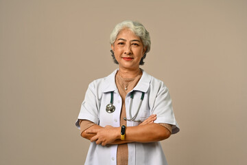 Confident senior woman doctor dressed in white overall with stethoscope isolated on brown background