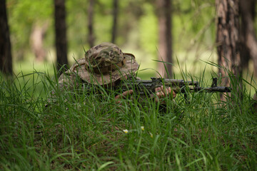 A soldier with a machine gun is lying in the grass, taking aim