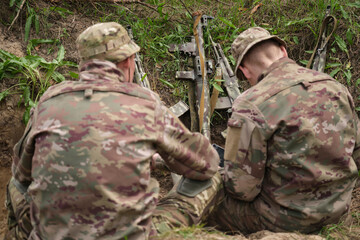 Soldiers work on a battle strategy in a notebook, against the background of weapons stacked in a...
