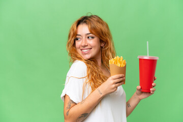 Young caucasian woman holding fried chips and soda isolated on green screen chroma key background  background