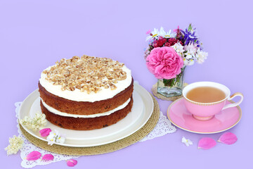 Carrot and walnut cake with cup of tea and summer flowers on purple background. Homemade delicious food concept for afternoon tea or birthday party.