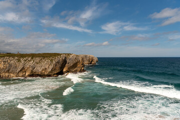 Panoramic view of the tourist beach of Guadamia on the coast of Asturias on its way out to sea with rough seas and some waves surrounded by cliffs on a sunny day.