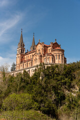 Fototapeta na wymiar Impressive panoramic view of the touristic basilica of Santa María la Real de Covadonga built of red stone on a hill in the foothills of the Picos de Europa in Asturias
