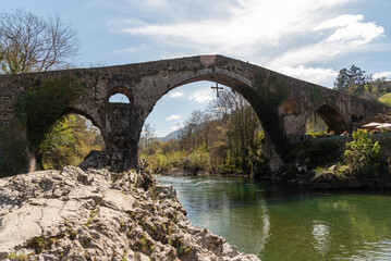 Fototapeta na wymiar Panoramic view of the Roman bridge in the tourist town of Cangas de Onís in Asturias, built over the river Güeña, surrounded by vegetation and nature.