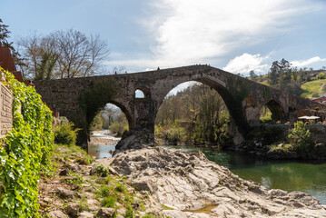 Fototapeta na wymiar View of the Roman bridge in the tourist town of Cangas de Onís in Asturias, built over the river Güeña, surrounded by vegetation and nature at sunset.