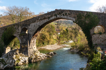 Fototapeta na wymiar Impressive view of the Roman bridge in the tourist village of Cangas de Onís in Asturias, built over the river Güeña, surrounded by vegetation and nature during the sunset