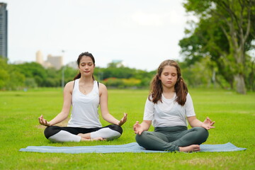 beautiful caucasian mom and little daughter practice yoga and pilates in the park outdoors. healthy lifestyle concept