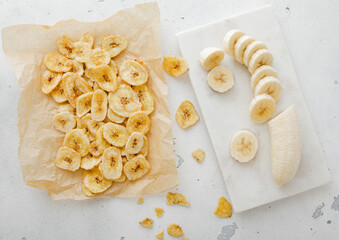 Fresh banana and baked crunchy chips snack on light kitchen background.