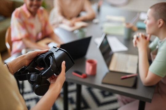 Close up of unrecognizable woman holding VR headset with blurred team meeting setting, copy space - Powered by Adobe