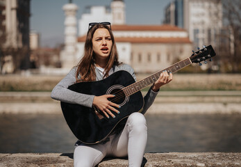 Gorgeous girl sitting by the quay. She is playing guitar and singing