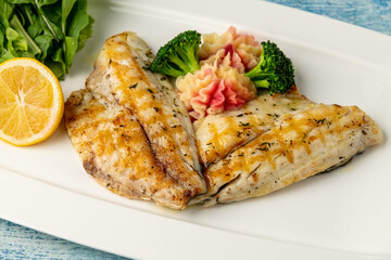 Grilled sea bream fillet with vegetables and greens on wooden table