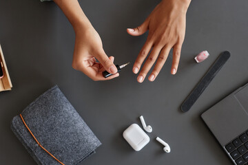 Minimal top view closeup of young woman doing manicure at desk with laptop and using nail polish, copy space