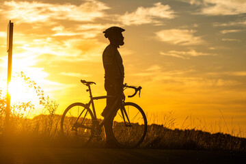 Fototapeta premium Sports and outdoor activities concept.Silhouette of cyclist riding a road bike on open road in evening during sunset.